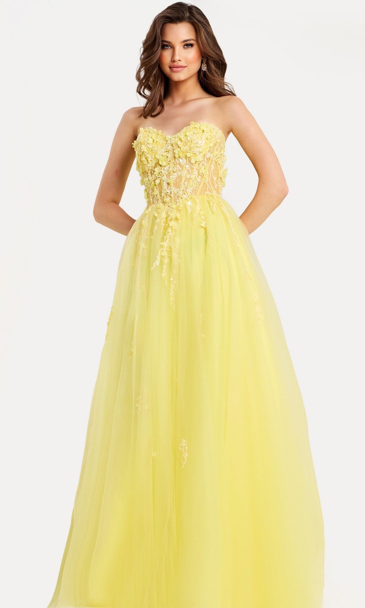 A woman models the yellow Jovani 49704 long prom dress, featuring a strapless floral-embellished bodice and flowing tulle A-line skirt, standing against a plain white background.